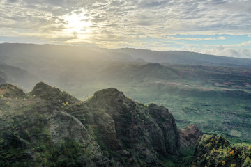 Cliff craggy terrain dropping away with green trees and shrubs at sunrise
