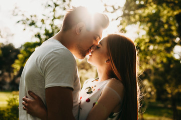 Side view portrait of a amazing caucasian couple kissing against golden hour light embracing while...