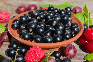 Ripe berry black currant in a ceramic plate with green leaves on a wooden table vintage, copy space, close-up