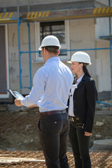 Two architects a man and a woman in construction in white helmets.