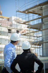 Two architects a man and a woman in construction in white helmets.