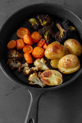 Roasted fried vegetables in a cast iron pan with potato, cauliflower, carrot and broccoli.  On a slate background.