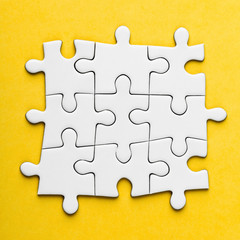 Fototapeta premium Connected blank puzzle pieces on a yellow background.
