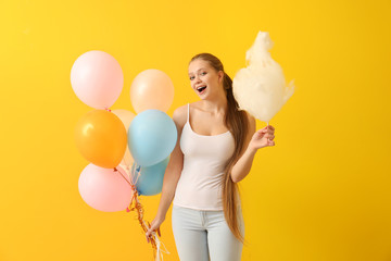 Beautiful woman with cotton candy and air balloons on color background
