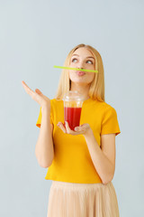 Funny young woman with fresh juice on light background