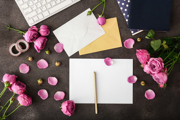 Beautiful pink roses with stationery and computer keyboard on dark background