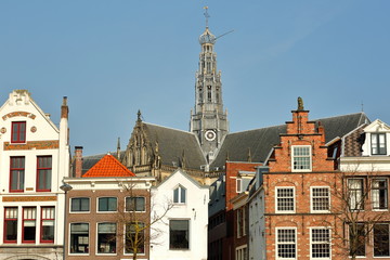 Traditional and colorful facades located along Spaarne river, with the clock tower of St Bavokerk Church in the background, Haarlem, Netherlands