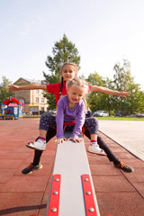 Two happy smiling caucasian girls having fun on playground, riding seesaw arms outstretched in...