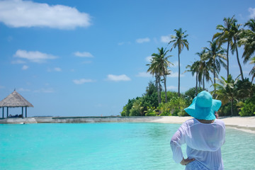 Fototapeta na wymiar a woman in a blue hat stands back on a beautiful paradise beach of the Maldives