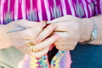 Hands close-up of an old lady knitting on knitting needles, using colorful wool.