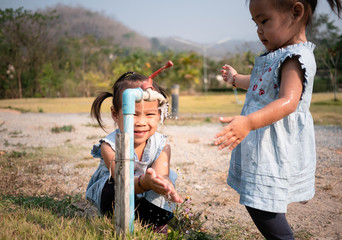 Asian little girl and sister washing her hands from steel faucets in the garden.