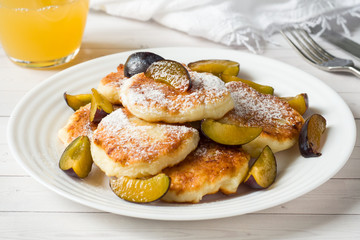 Cheese pancakes in powdered sugar with fresh plums on a plate