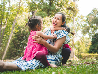 Fototapeta premium Asian mother and her daughters playing together on grasses ground in the park so happily.