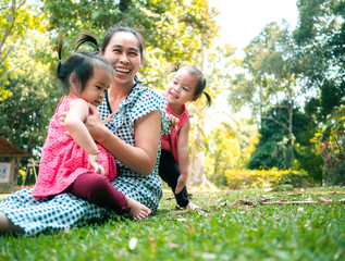 Fototapeta premium Asian mother and her daughters playing together on grasses ground in the park so happily.