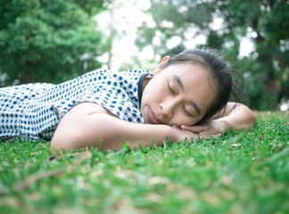 Naklejka na ściany i meble Asian young woman lying down on grass ground in the park for relaxation time. Space for your text.