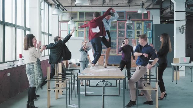 Colleagues celebrate the end of the work week, have fun dancing on the table and throw up paper. Success. Corporate party business team. Modern trendy office interior. Co-workers entertainment
