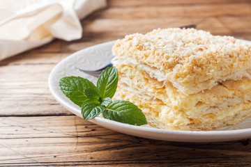 Layered cake with cream Napoleon millefeuille vanilla slice with mint on wooden background.