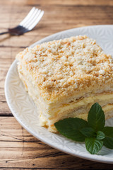 Layered cake with cream Napoleon millefeuille vanilla slice with mint on wooden background.