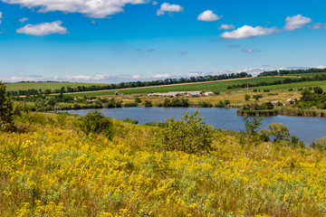 Summer landscape with beautiful lake, green meadows, hills, trees and blue sky