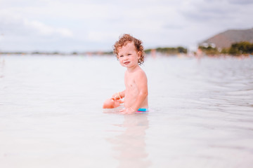 Fototapeta na wymiar Cute little curly baby play on beach.