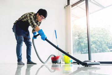 Young attractive man is cleaning vacuum commercial cleaning equipment on floor at home helping wife.