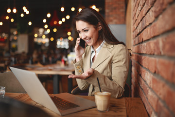 Attractive businesswoman sitting at working friendly cafe and using smart phone.