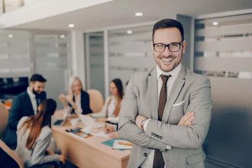 Fotobehang Handsome smiling businessman in formal wear and eyeglasses standing at boardroom with arms crossed. Love and respect do not automatically accompany a position of leadership. They must be earned © dusanpetkovic1