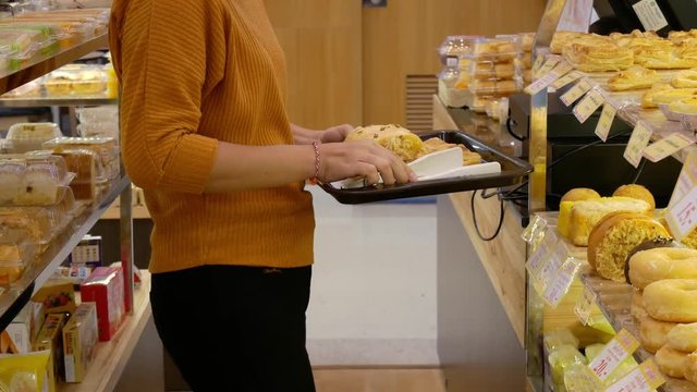 April 2019, Asian young woman in casual clothes is walking in bread shop in the supermarket and pick up bread place down on the tray and walking to pay money at cashier.