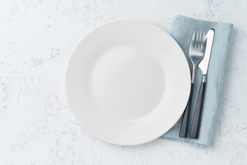 clean empty white plate, fork and knife on white stone table, copy space, mock up, top view.