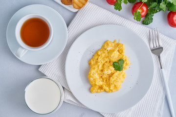 Breakfast with pan-fried scrambled eggs, cup of tea, glass of milk, tomatoes on white background. Omelette, top view