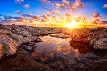 Amazing nature landscape, colorful sunset on the white rocks with sun, blue sky, clouds and reflection in the water, Cyprus. Outdoor travel background