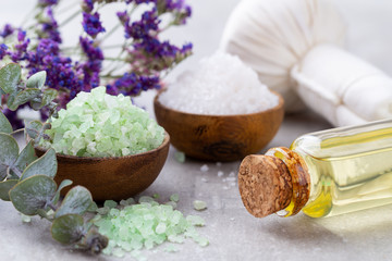 Sea salt in bowl, aroma oil in bottles, Wellness and flowers on grey textured background and flowers on vintage wooden background. Selective focus.