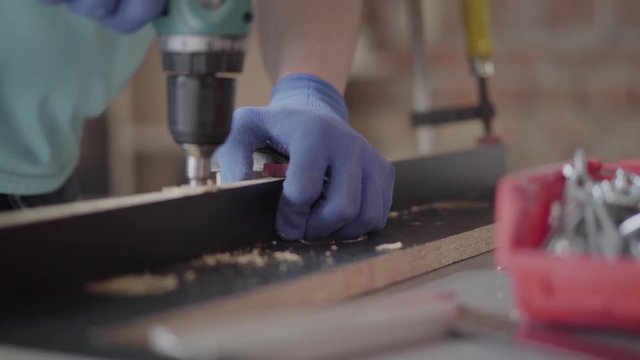 Unrecognized craftsman making halls in the chipboard details with cordless screwdriver. Concept of hand manufacturing. Craftman works in a workshop.