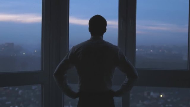 Back view of the thoughtful businessman wearing a suit looking out of the panoramic window. slow motion. 3840x2160
