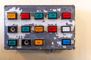 A small old control panel showing buttons of various colours on old paint peeling panel, nobody in the image