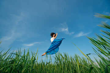 Flying dancer in the air. Happy woman ballerina in blue fabric skirt making a big jump on Green field. Summer or Spring concept 