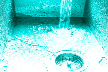 Flow of water in a metal sink on a modern kitchen. Toned