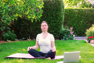 Beautiful young woman practicing yoga in garden outdoors following guide of online tutorial or...