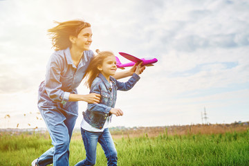 Young woman and girl in denim clothes having fun with small plane on green lawn in summer day