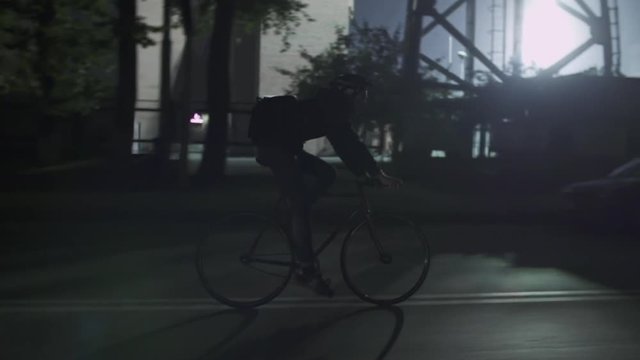 Cyclists at night city street. Men ride fixed gear bicycles. Active lifestyle. Silhouettes of city travellers on eco-friendly urban transport. Defocused lights, traffic, bokeh on background.