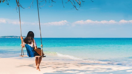 Happy Asian woman sitting on a swing on the white sand beach by the blue sea background in summer of Thailand.Travel in holidays concept. - obrazy, fototapety, plakaty