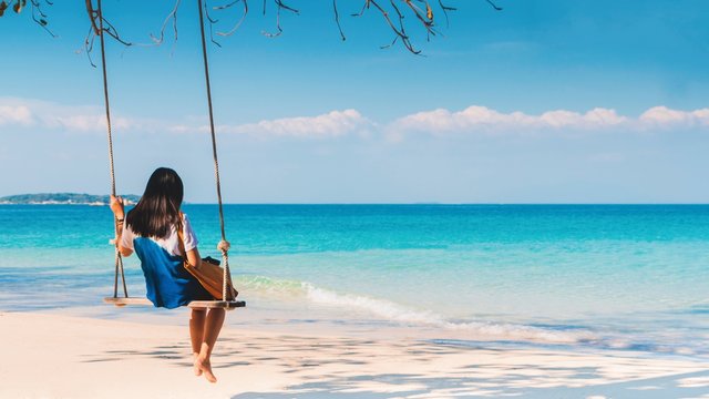 Happy Asian woman sitting on a swing on the white sand beach by the blue sea background in summer of Thailand.Travel in holidays concept. - Powered by Adobe