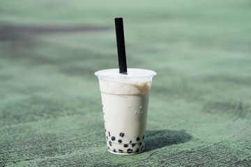 Bubble Milk Tea - Holding a plastic glass of fresh milk with black pearl (boba) on green background, Taiwanese style.