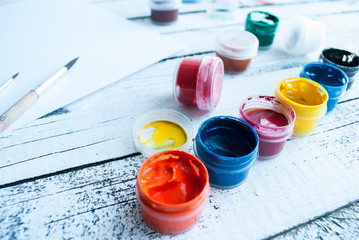 Open gouache jars and a blank blank with brushes for painting on a wooden white background