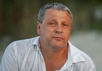 Portrait of a mature man in white summer shirt against nature background