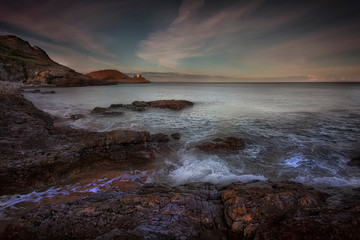 High tide over the rocks at dusk on Bracelet Bay and Mumbles Lighthouse on the Gower peninsula in Swansea, South Wales, UK.