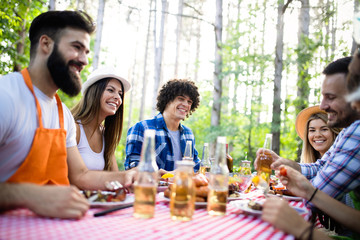 Group of happy friends eating and drinking beers at barbecue dinner