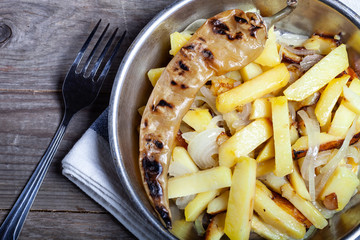 Delicious roast potatoes with onion and spices in a pan on kitchen towel on the old wooden table. Traditional rural dinner
