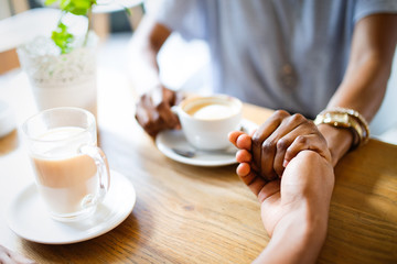 Close-up of couple holding hands while sitting together in cafe with coffee cups on the table