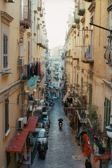 Narrow street in Naples with old houses, Italy. Motorbike driving along the alleyway. Linen hanging on the balconies